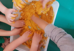 Ręce dzieci zanurzone są w misce. Ugniatają masę z dyni i mąki ziemniaczanej.